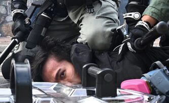 Immagine di un attivista bloccato a terra da poliziotti con manganelli